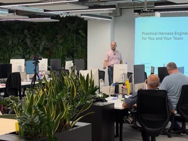 Jaroslav Pantsjoha presenting at Digital Futures in London, beside a projected slide titled "Practical Harness Engineering for You and Your Team", with attendees at desks in the foreground and a living plant wall behind.